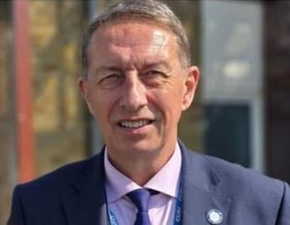 Image shows a man wearing a suit looking into the camera
